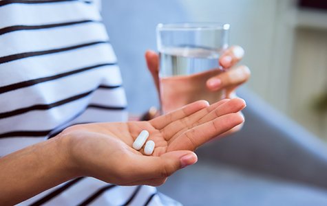 Close up of person holding glass of water and pain medication