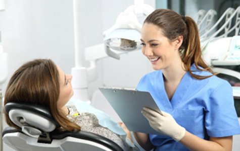 Dental assistant smiling while taking notes on clipboard