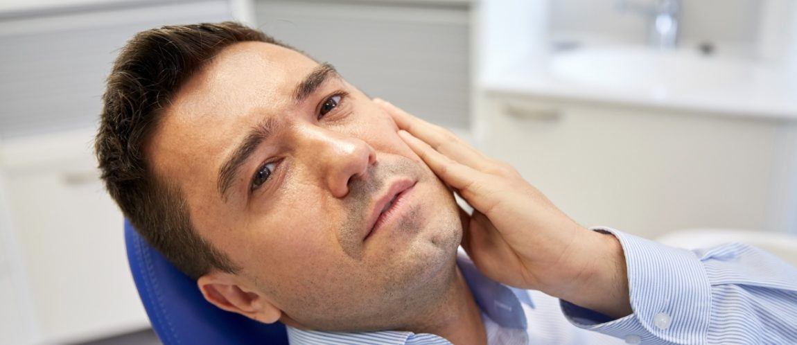 Man with impacted wisdom tooth holding jaw in pain
